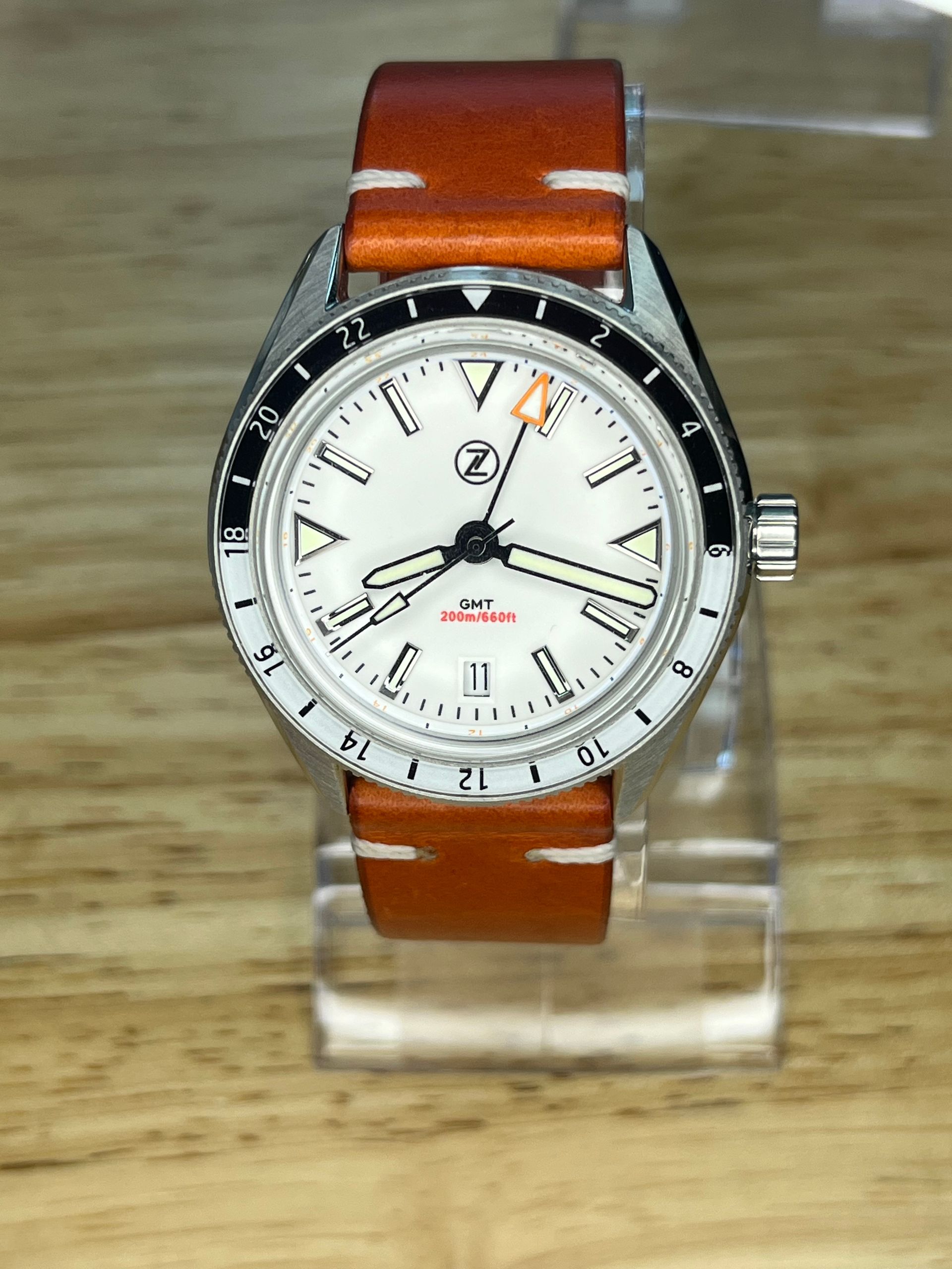 Cream-dialed wristwatch with black and white bezel, on a brown leather strap.