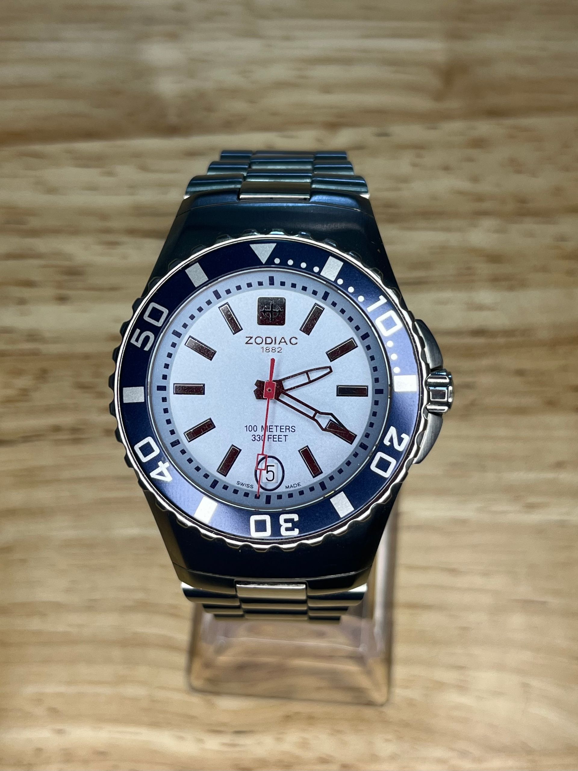 Silver watch with white face, blue bezel, and metal band on a wooden surface.