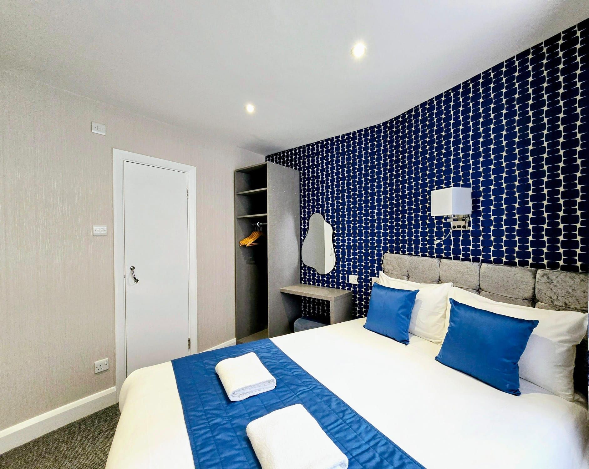 A hotel room with a king size bed and blue and white pillows.