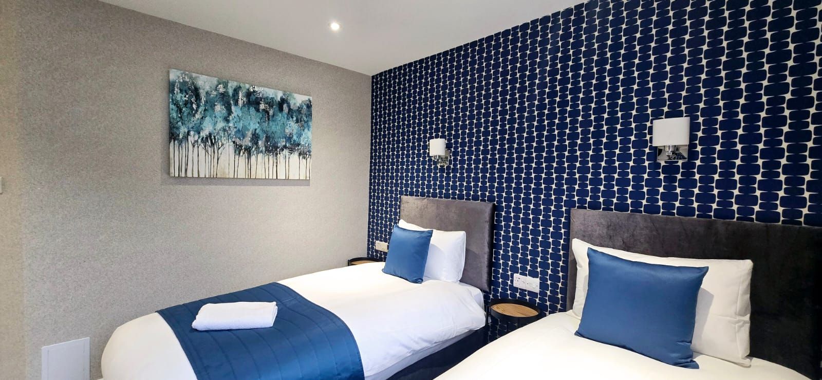 Twin beds with blue and white bedding, art, and patterned blue wall.