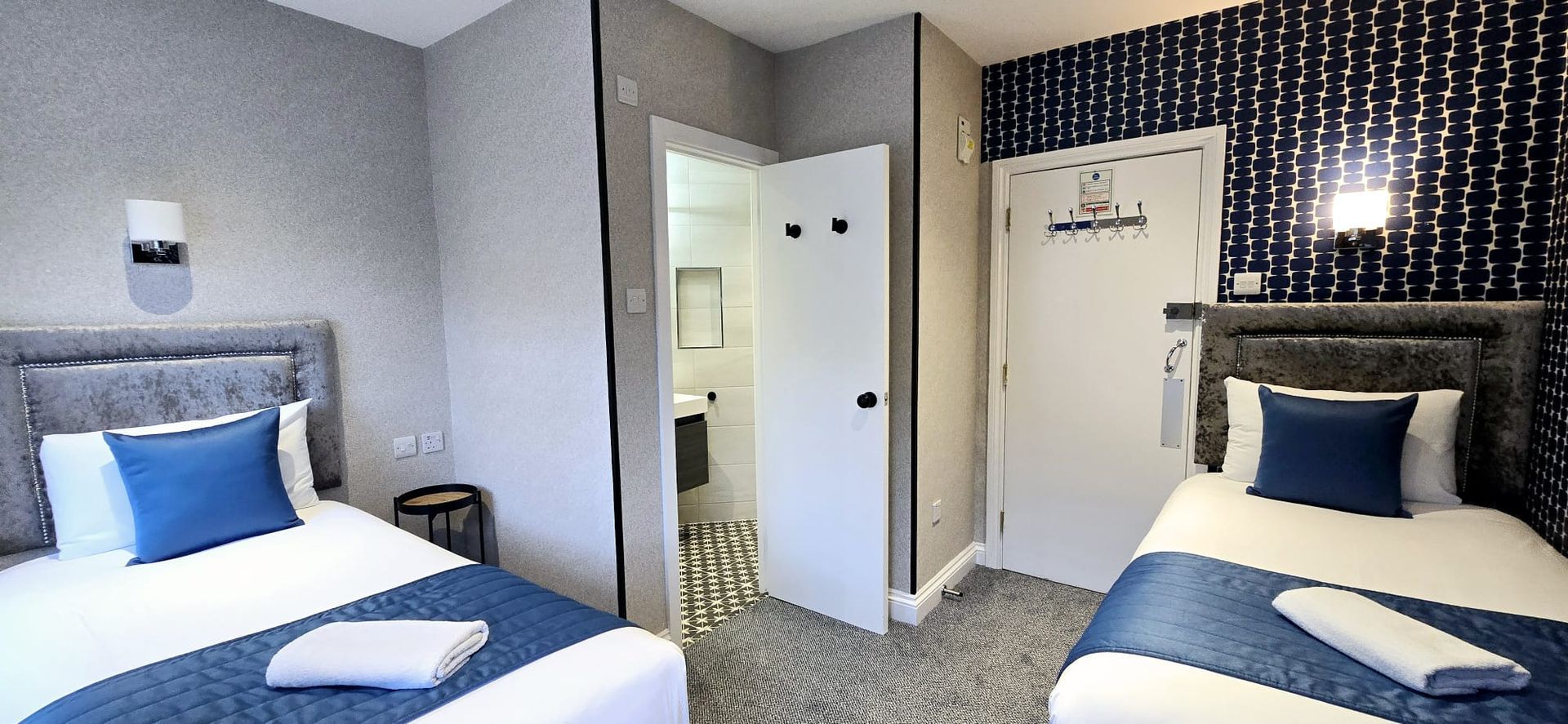 Two single beds in a hotel room with a bathroom and blue accents.