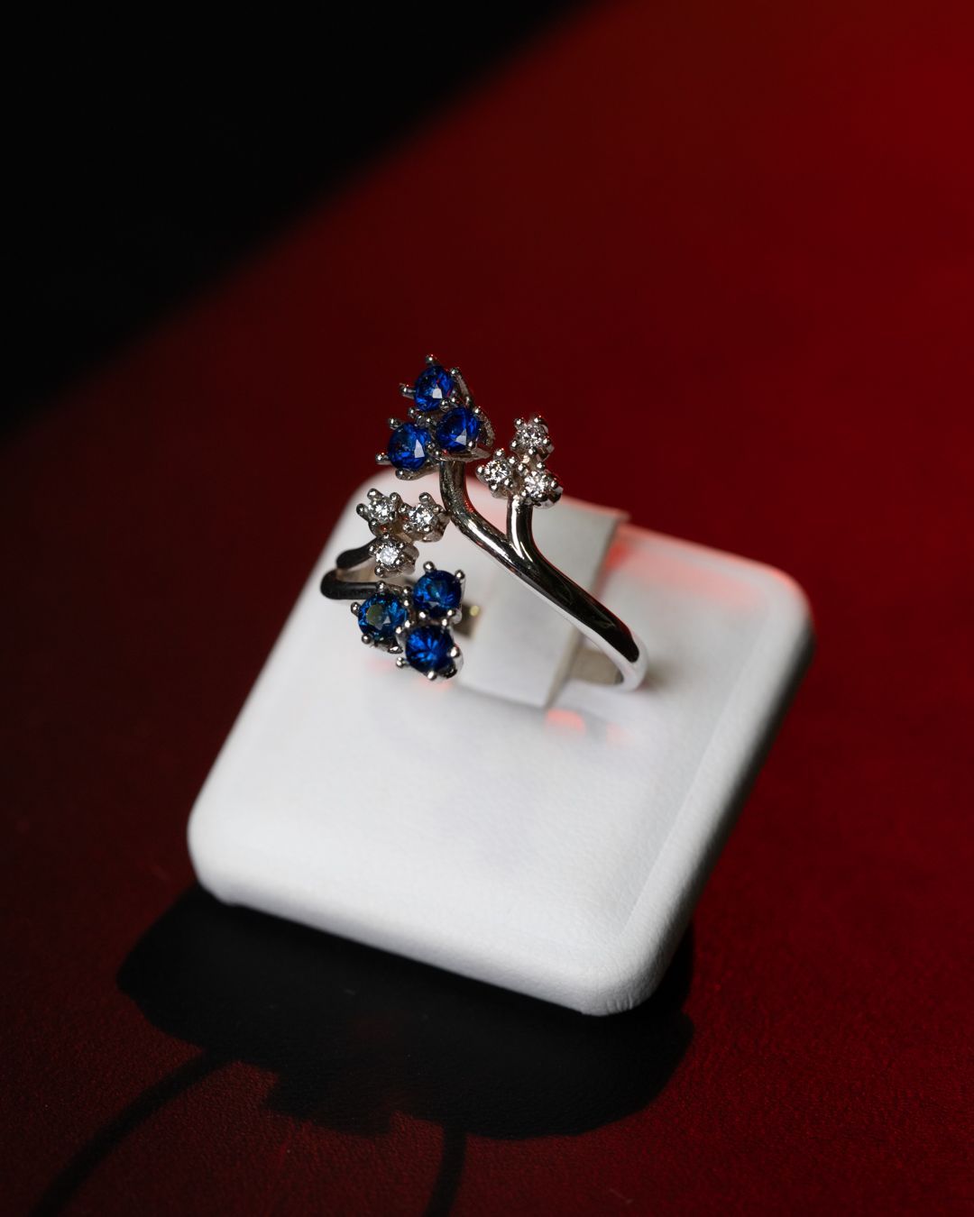 Un anello d'argento con pietre blu e bianche su un porta-anello bianco