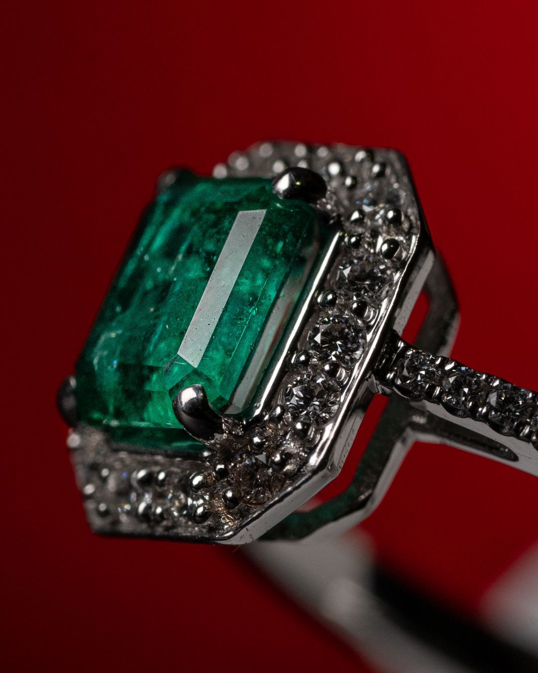 Un anello con uno smeraldo e diamanti su uno sfondo rosso