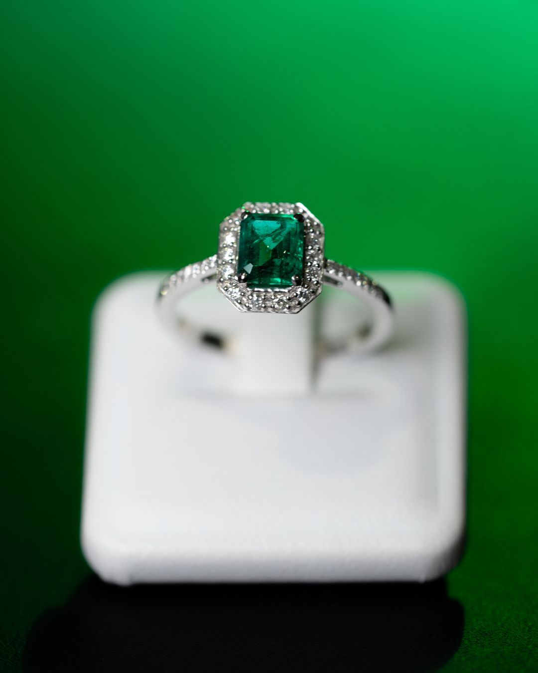 Un anello con smeraldo e diamanti è esposto in una teca bianca.