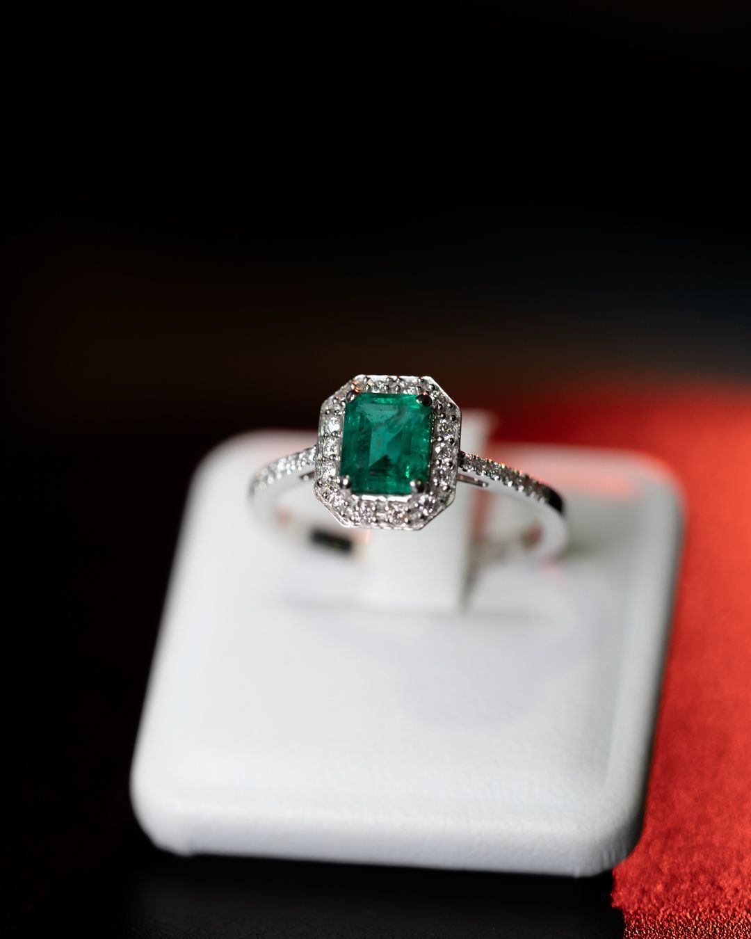 Un anello con smeraldo e diamanti è esposto in una teca bianca.