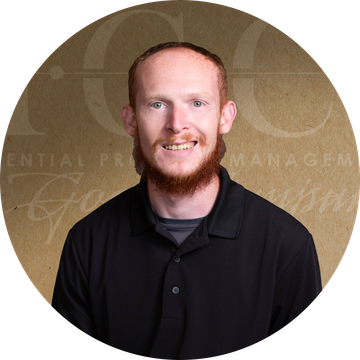 Man with red beard smiles, wearing a black shirt, in front of a golden background with text.