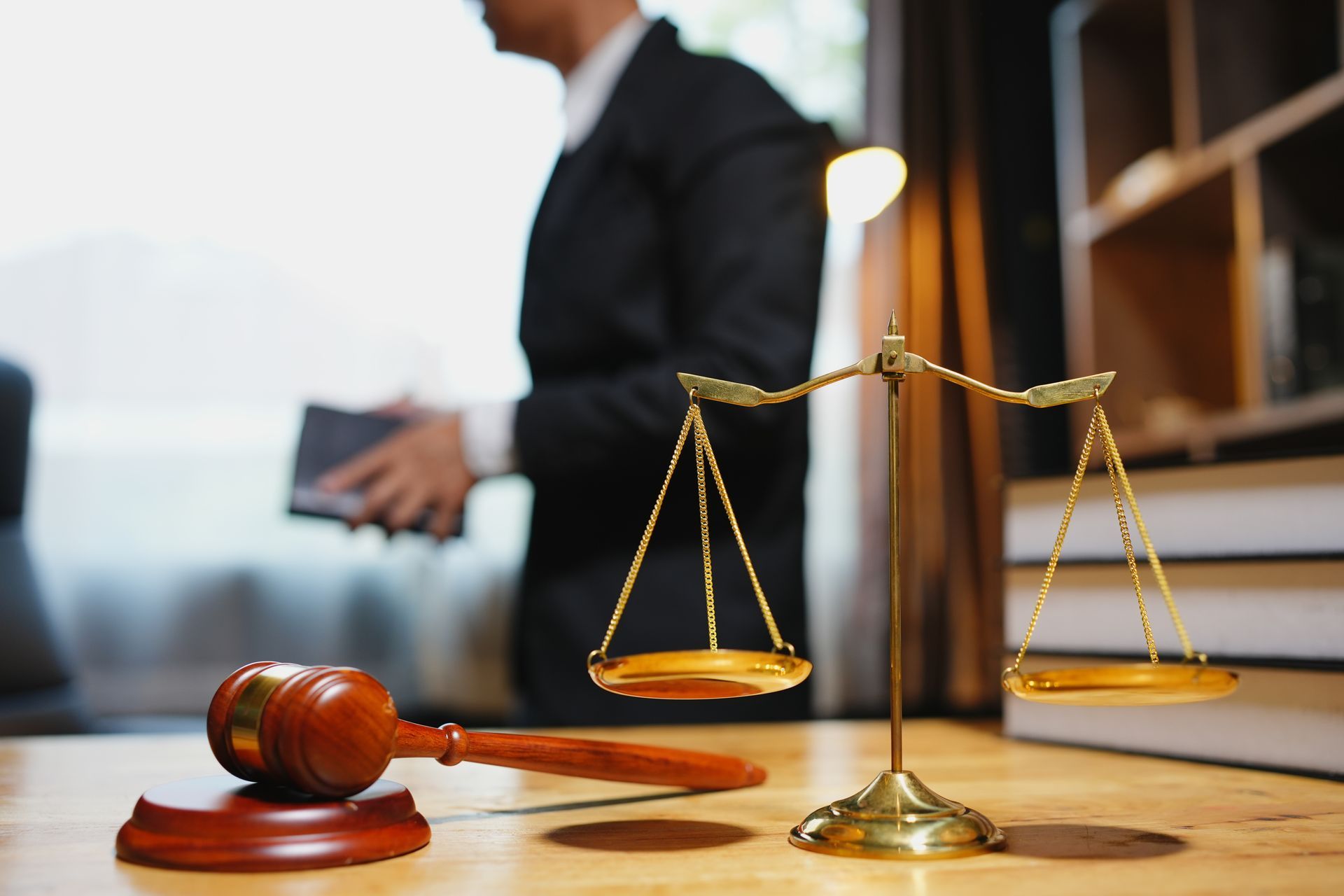 Gavel and brass scales on a desk, with a blurred lawyer in a courtroom background