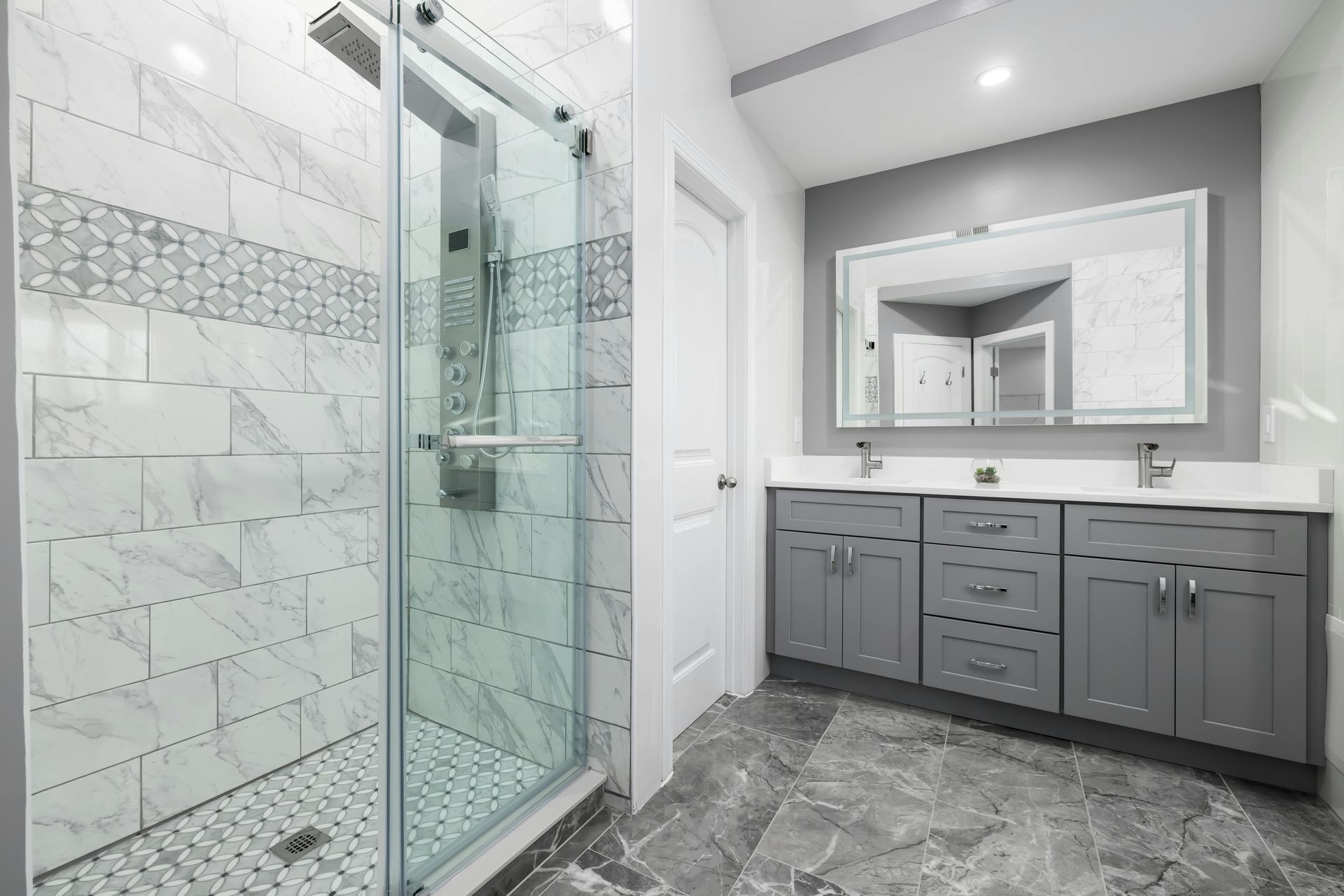 Modern bathroom with glass shower, gray vanity, large mirror, and marble tile flooring