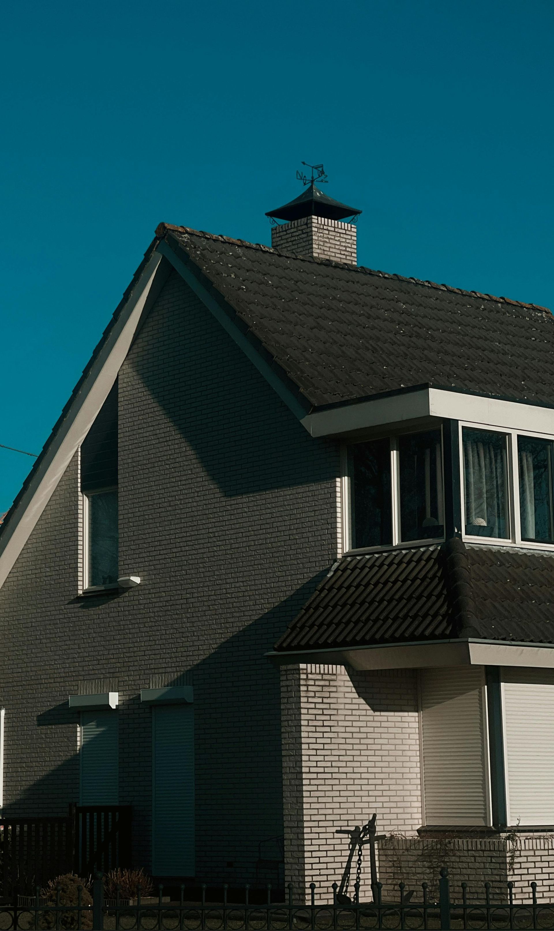 Two-story house with gray shingled roof and white siding against a blue sky