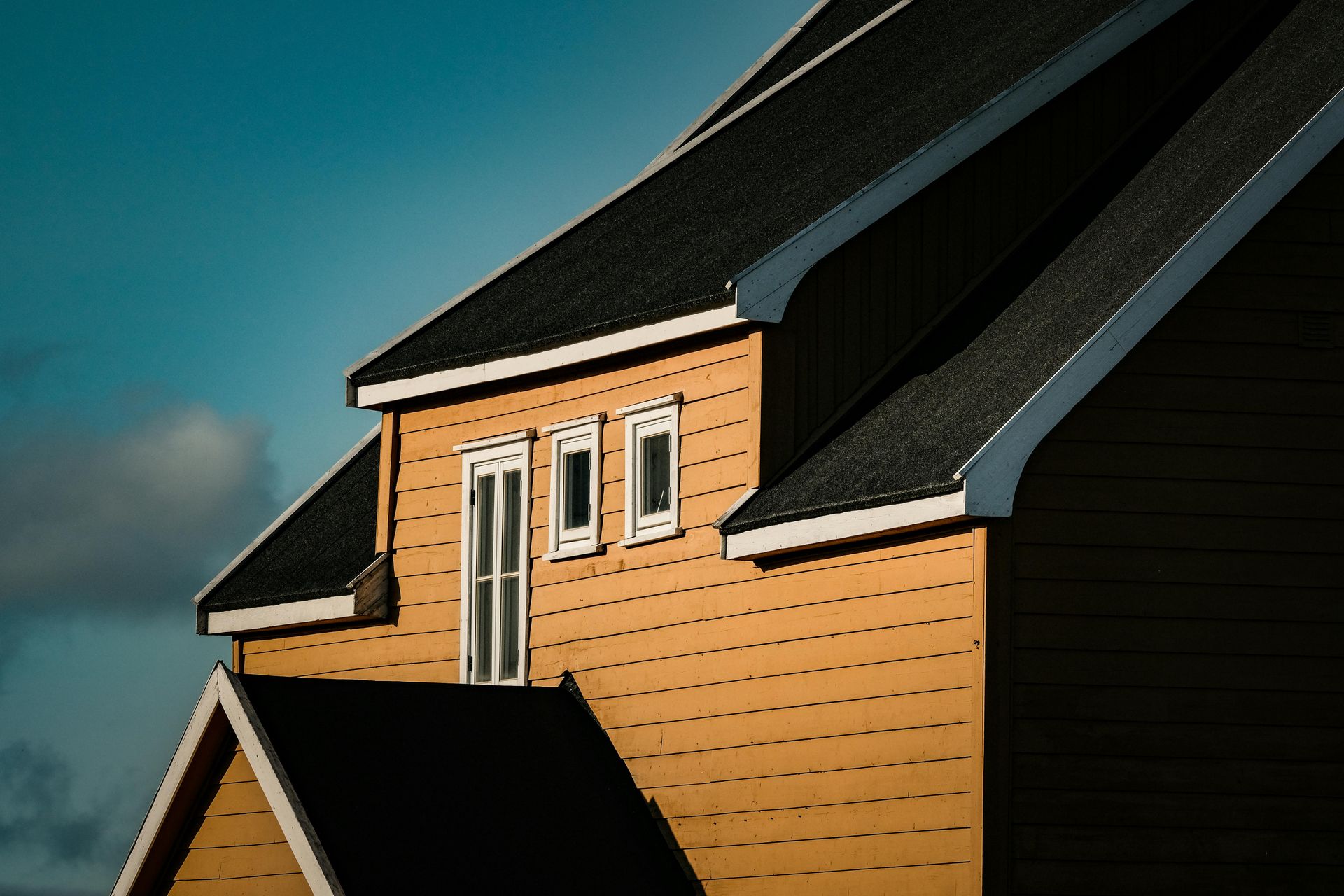 Tan house roof with black shingles and white trim against a blue sky