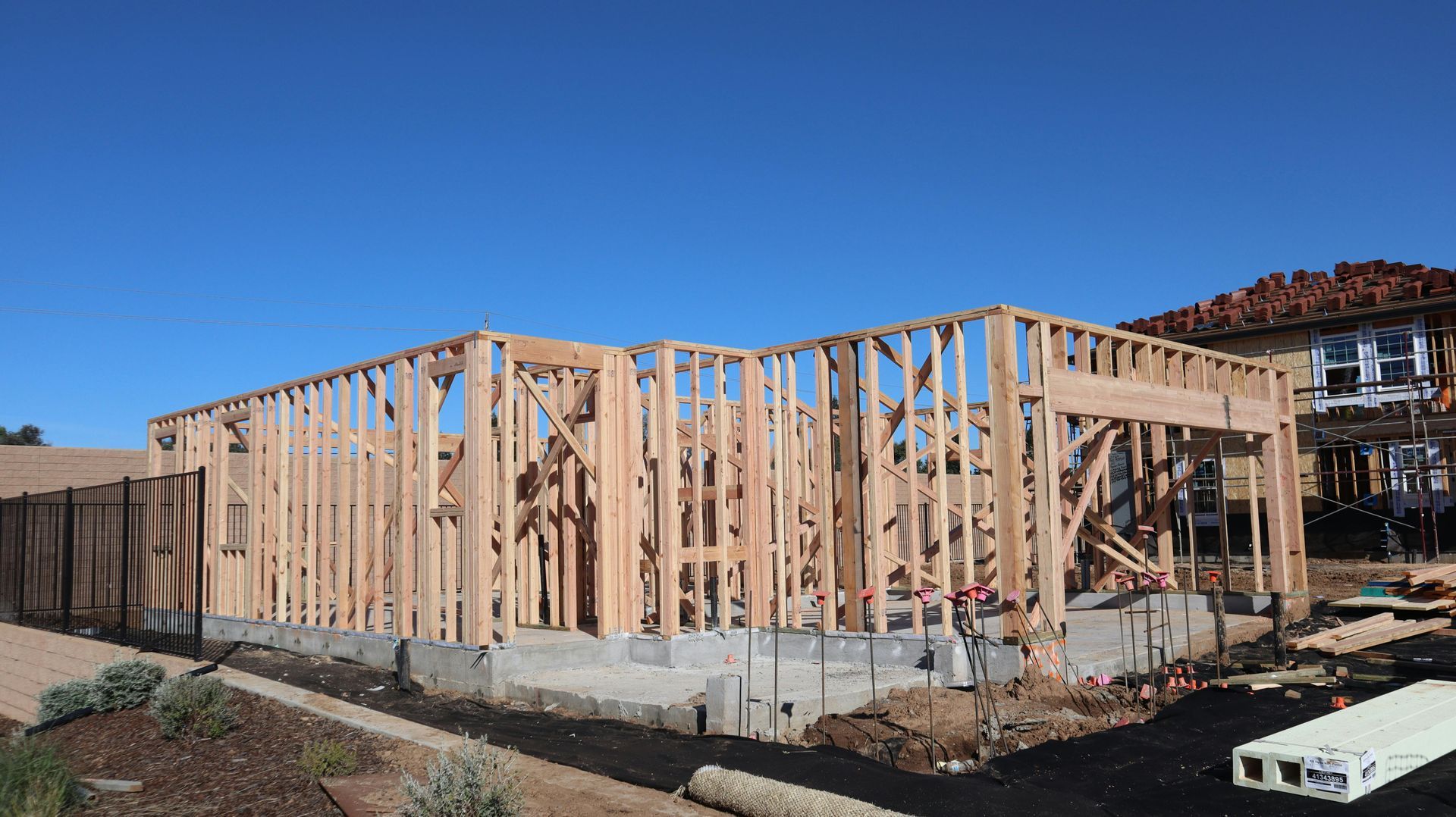 Wood-framed house under construction on a concrete foundation under a clear blue sky