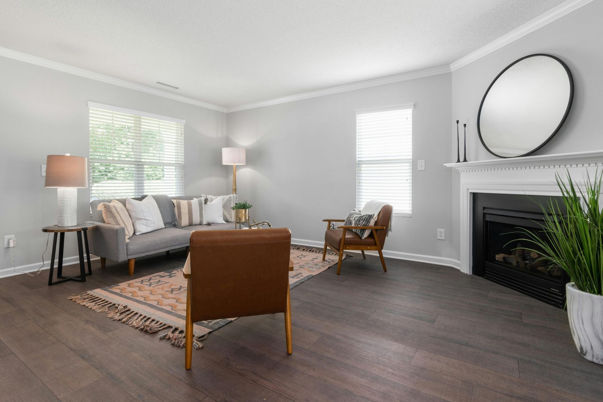 Bright living room with gray sofa, tan chair, rug, floor lamps, fireplace, and large mirror