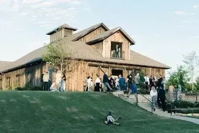 Burleson Electrician -A rustic barn hosts a lively gathering, with guests mingling outside. A child rolls on the grass in the foreground, adding a playful touch.