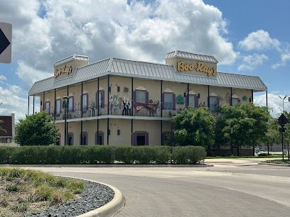 Burleson Electrician -A round black picnic table with attached seats is set on lush green grass, surrounded by leafless trees under a clear blue sky.