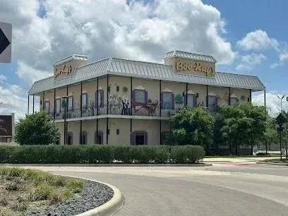 Burleson Electrician -A beige, two-story building with a wraparound balcony and lush greenery, under a blue sky with clouds. The tone is calm and inviting.