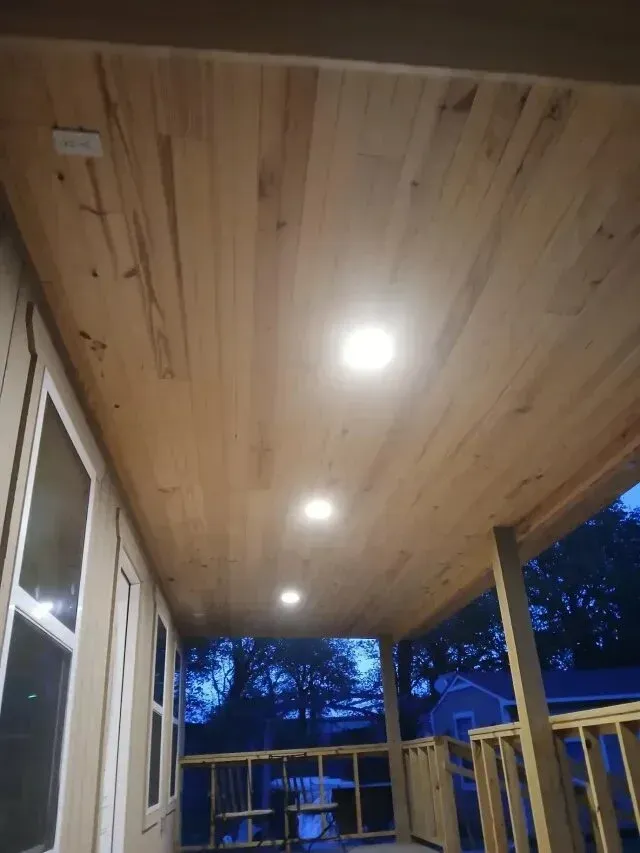 Burleson Electrician - Newly finished wood plank porch ceiling featuring three recessed circular lights overlooking a dark, twilight outdoor scene.