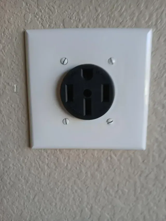 Burleson Electrician -A close-up of a black electrical outlet mounted on a white wall plate with two visible screws for installation.