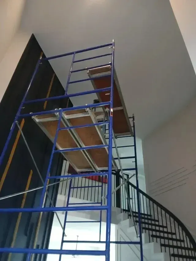 Burleson Electrician - Blue scaffolding towers next to a curved staircase inside a building with high ceilings, likely for painting or construction work.