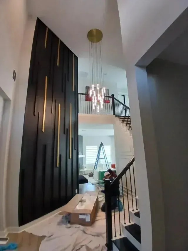 Burleson electrician - Modern foyer featuring a black accent wall with gold details, a stylish pendant light, and ongoing renovation with a worker and tools.