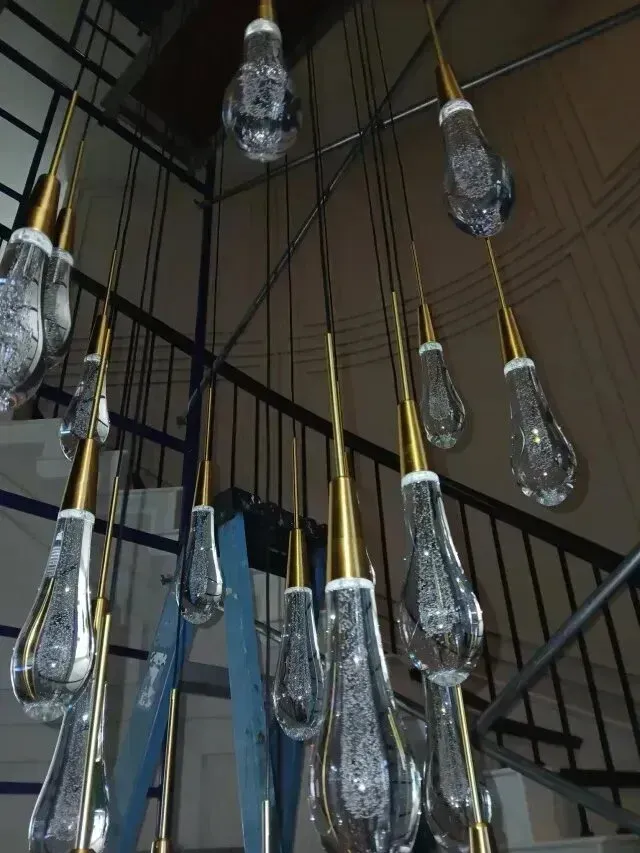 Burleson electrician - A modern chandelier made of elongated glass drops with gold accents, suspended above a blue ladder in a stylish interior.