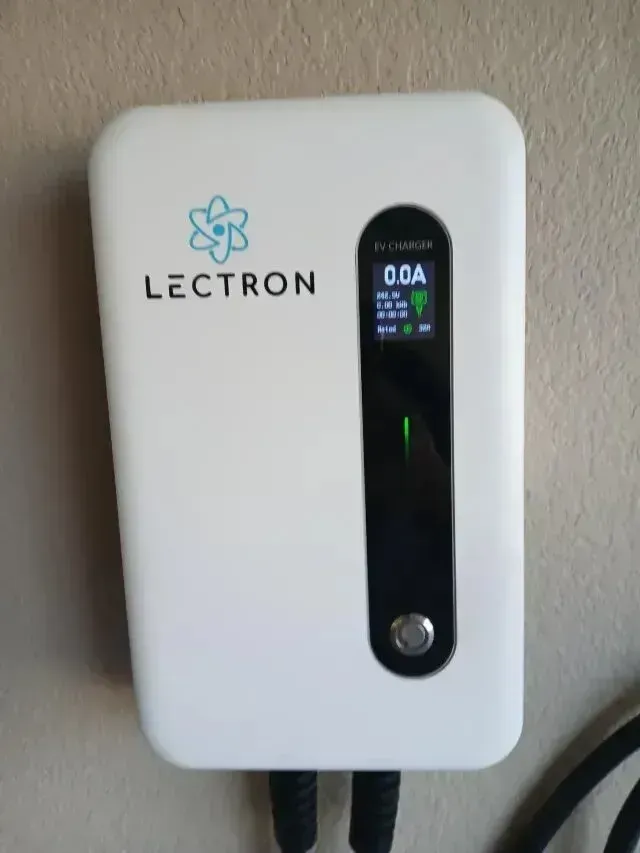 Burleson electrician - A white EV charger mounted on a wall, displaying a digital screen with a reading of 0.0A, surrounded by two charging cables.