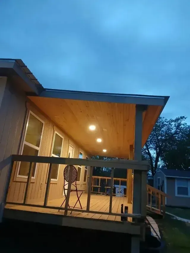 Burleson electrician - A cozy porch with warm lighting, wooden flooring, and a folding chair under a cloudy sky, creating a welcoming evening atmosphere.