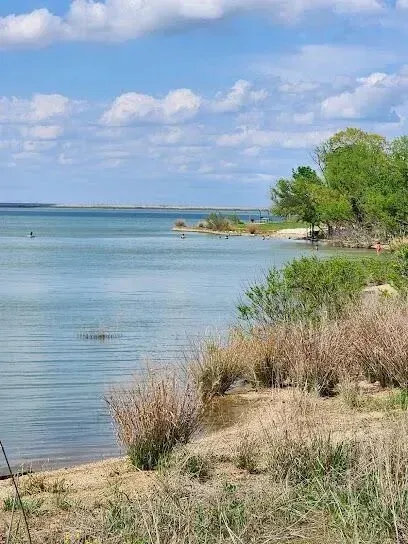 Burleson Electrician - Calm lake scene with clear blue water, surrounded by dry grass and lush green trees. The sky is partly cloudy, creating a serene atmosphere.