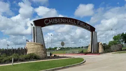 Burleson Electrician -Entrance archway to Chisenhall Fields with text on top, surrounded by manicured lawns and a bright blue sky with clouds.