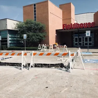 Burleson Electrician -A round black picnic table with attached seats is set on lush green grass, surrounded by leafless trees under a clear blue sky.