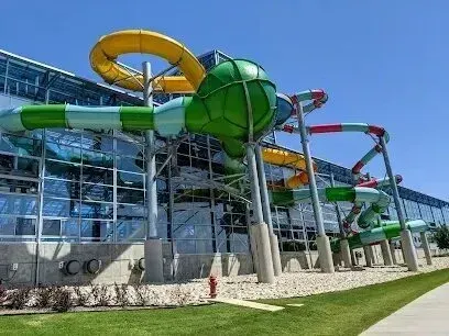 Burleson Electrician -Colorful outdoor water park slides with yellow, green, and red tubes arching against a large modern building with glass windows under a clear blue sky.