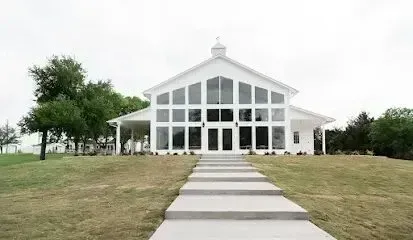 Burleson Electrician - Wide, white chapel with large glass windows and a symmetrical design stands at the top of a grassy hill, bordered by trees, creating a serene ambiance.