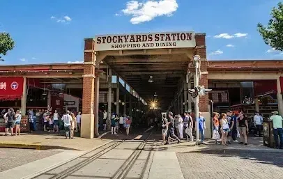 Burleson Electrician -Exterior view of the Stockyards Station building with a prominent sign, showing pedestrians near railroad tracks on a sunny day.