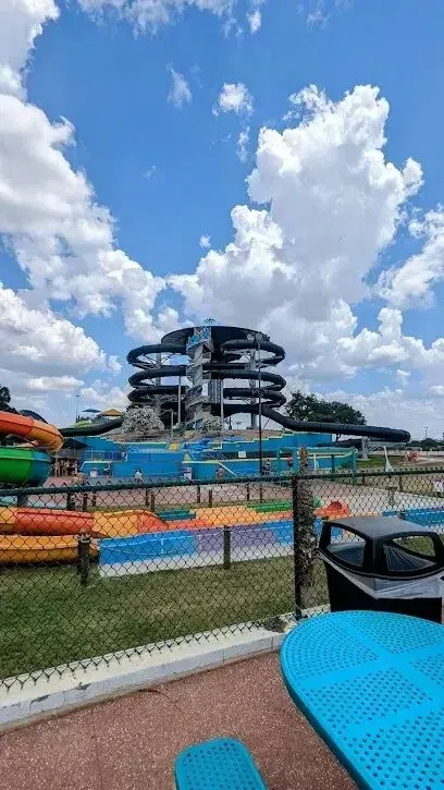 Burleson Electrician - Towering black spiral waterslides dominate a vibrant water park scene under a bright blue sky with fluffy clouds, creating a lively summer atmosphere.