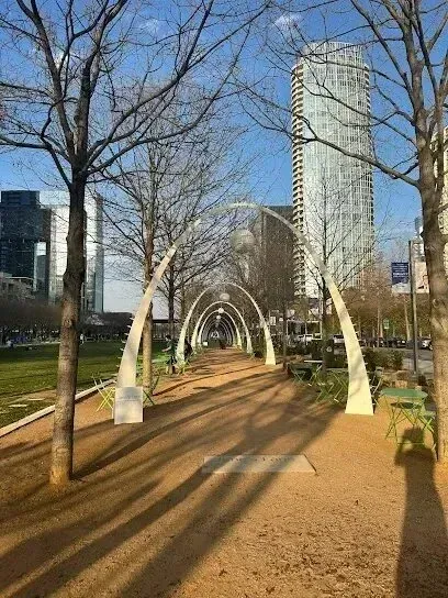 Burleson Electrician - Tree-lined walkway with metal arches under a clear blue sky. Green chairs and tables are scattered along the path, creating a serene, inviting atmosphere.