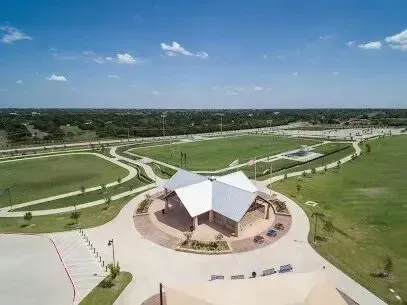 Burleson Electrician - Aerial view of a park facility with a white-roofed building centered among winding paths and lush greenery under a clear blue sky with scattered clouds.