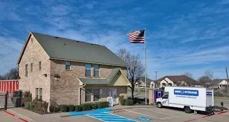Burleson Electrician - Image of a brick building under a blue sky with an American flag. A white moving truck is parked near a blue accessible parking space.