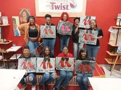 Burleson Electrician -A group of nine smiling women stands in a paint studio holding paintings of red high heels. The mood is joyful and creative, with diverse expressions.