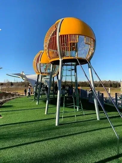 Burleson Electrician - Two bright yellow, spherical climbing structures stand on metal posts above green turf under a clear blue sky at a modern playground.