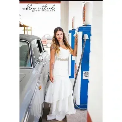 Burleson Electrician - A bride in a white, one-shoulder wedding gown with a jeweled belt stands between a vintage silver car and two bright blue vintage gas pumps.