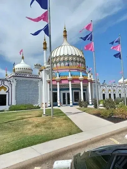 Burleson Electrician - Ornately domed, colorful structure with numerous pink and blue flags flying against a bright blue sky, viewed from a foreground parking area.