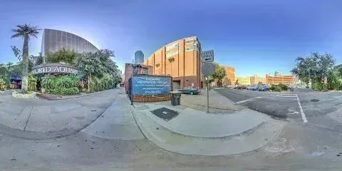 Burleson Electrician - Panoramic view of an aquarium entrance with palm trees, a sign for a nearby music venue, and surrounding urban buildings under a clear blue sky.