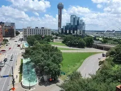 Burleson Electrician - Aerial view of a cityscape with a tall tower, modern buildings, lush green park, winding road, and a canal, under a blue sky with fluffy clouds.