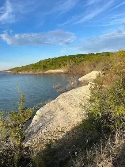 Burleson Electrician - A serene lakeside scene with a rocky shoreline, clear blue water, and lush greenery under a wide, partly cloudy sky. The atmosphere is calm and peaceful.