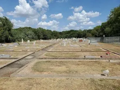 Burleson Electrician -Grassy cemetery with scattered headstones under a partly cloudy blue sky. Trees line the background, creating a serene and reflective atmosphere.