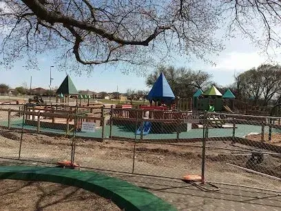 Burleson Electrician - A fenced-off playground under construction with colorful play structures and a bare tree branch overhead, set against a clear blue sky.