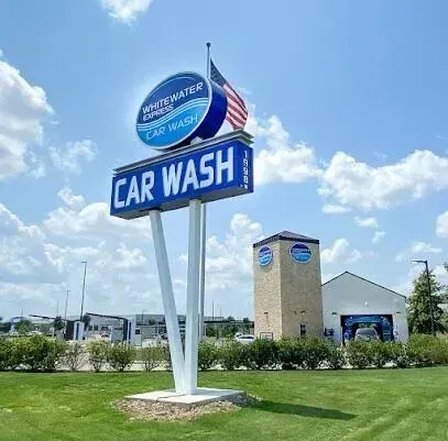 Burleson Electrician - Tall car wash sign with an American flag stands against a bright blue sky and fluffy clouds. Nearby, a building with blue signage emphasizes a clean, inviting look.
