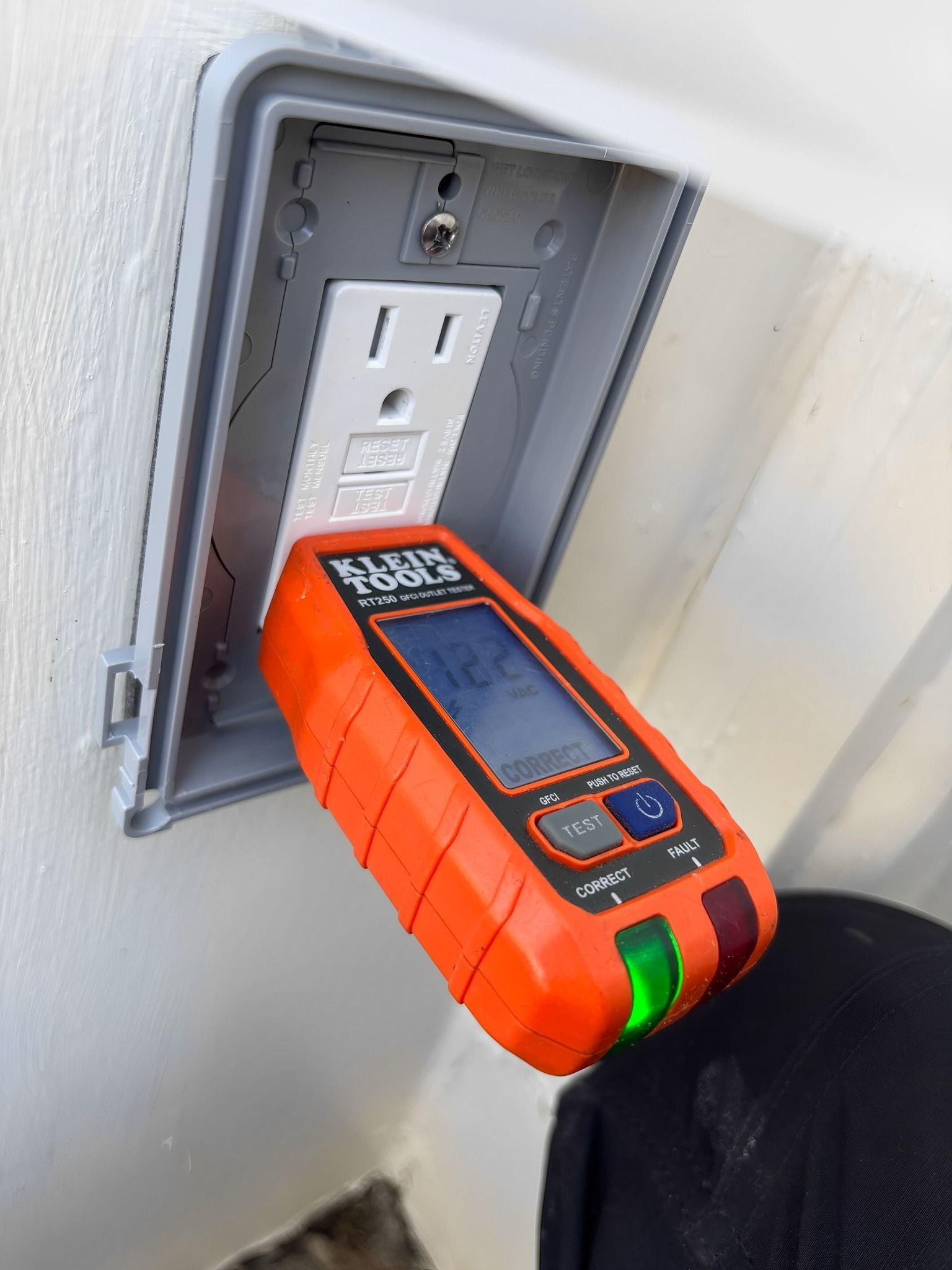 Orange electrical outlet tester plugged into a white GFCI outlet; green light indicates proper wiring.