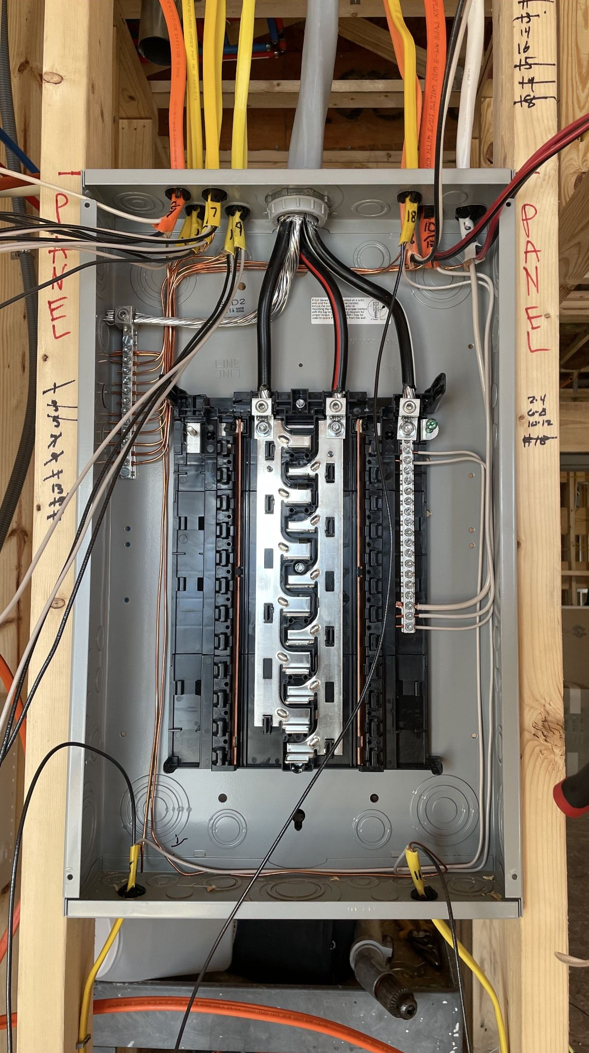 Electrical panel with wires and circuit breakers installed inside a wooden frame.