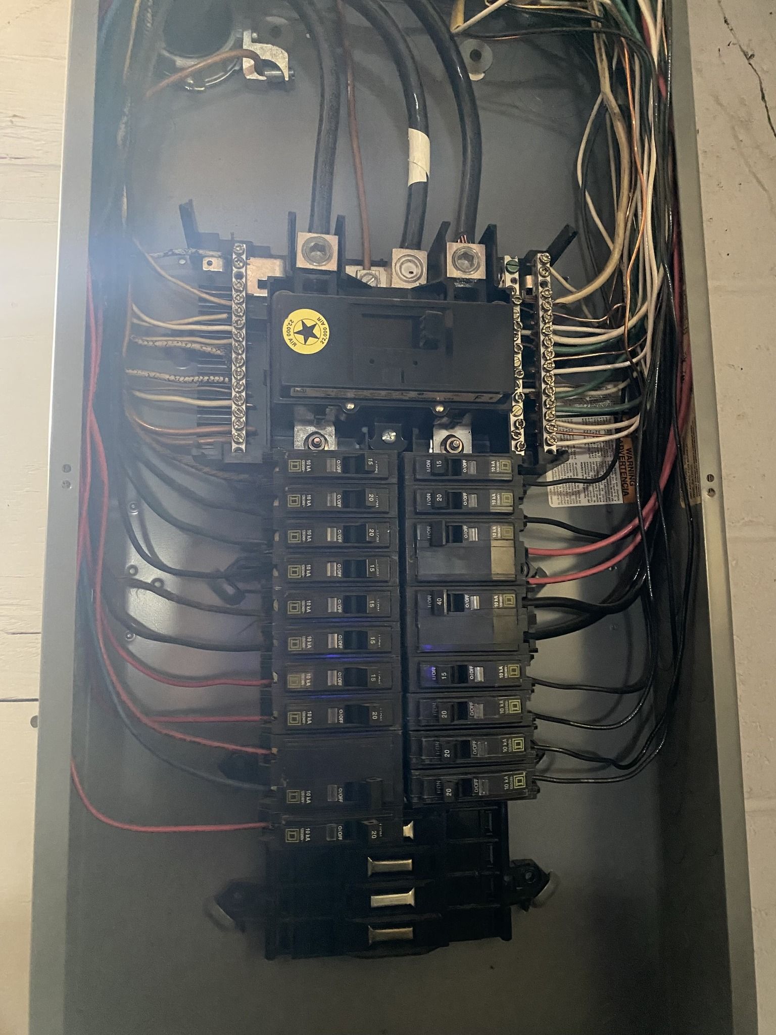 Electrical panel with numerous circuit breakers and wiring inside a metal enclosure.