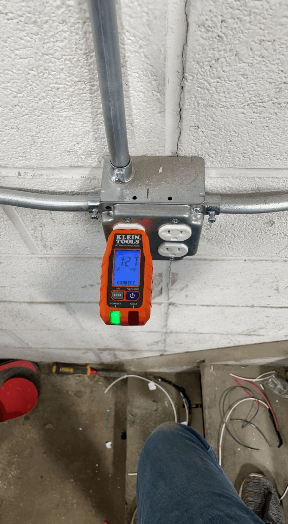 Electrical outlet box with a stud finder attached. Conduit and a concrete wall are visible.